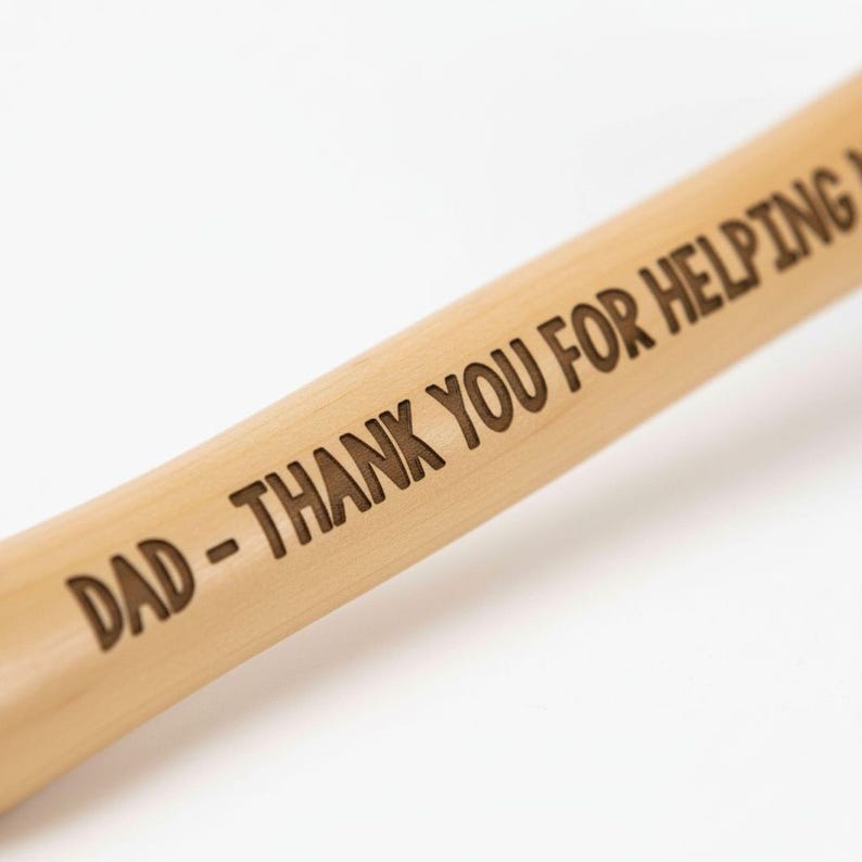 A wooden stick with the words "DAD - THANK YOU FOR HELPING" engraved on it.