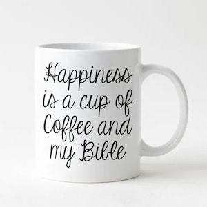 A white ceramic mug with black text that reads "Happiness is a cup of coffee and my Bible".
