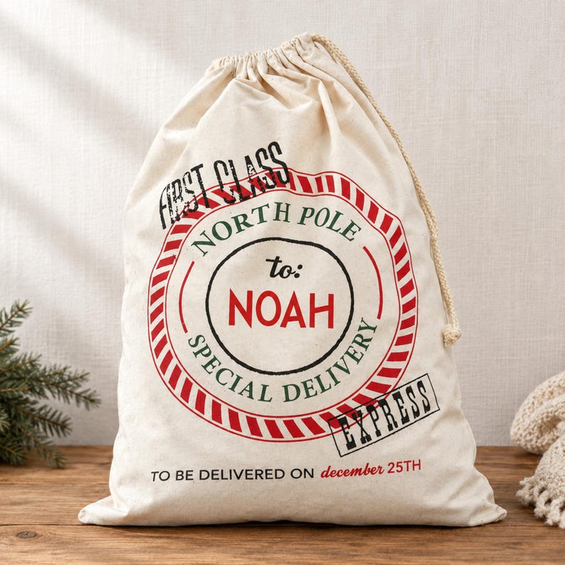 May include: A cream-coloured canvas drawstring gift sack featuring a red and green circular stamp design. The text reads: FIRST CLASS NORTH POLE to: NOAH SPECIAL DELIVERY EXPRESS TO BE DELIVERED ON december 25TH. The bag has a beige rope closure.