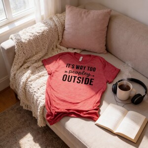 a cozy scene with a red t-shirt, a mug of coffee, a pair of headphones, and an open book on a couch.