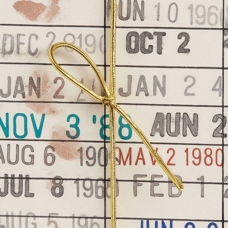a close-up view of a calendar page with a gold ribbon tied around it. The calendar page displays various dates and months, including "UN" and "JAN" among others.