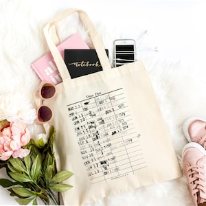 a beige tote bag with a printed date due list, a pair of sunglasses, a pink notebook, a smartphone, and a pair of pink sneakers, all arranged on a white fur rug.