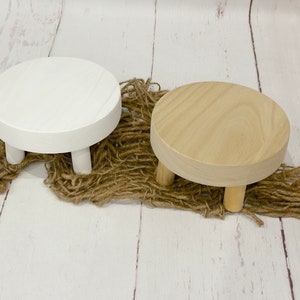 Puede incluir: Dos soportes de exhibici&oacute;n de madera con tres patas cada uno. Un soporte es blanco y el otro es de madera natural.
