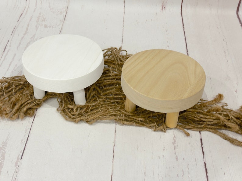 Puede incluir: Dos soportes de exhibici&oacute;n de madera con tres patas cada uno. Un soporte es blanco y el otro es de madera natural.