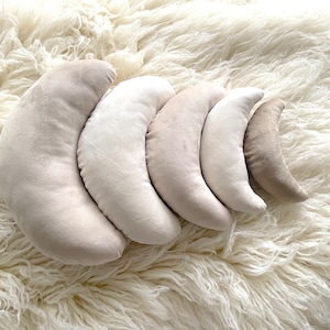 May include: Set of five crescent-shaped pillows in various shades of beige and cream. The pillows are arranged in a row, with the largest pillow at the bottom and the smallest pillow at the top.