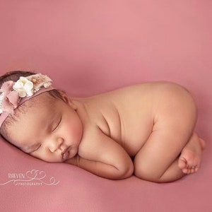Pu&ograve; includere: Una neonata dorme su uno sfondo rosa. Indossa una fascia rosa con fiori bianchi e pizzo.