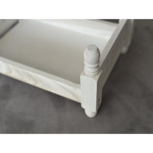 Puede incluir: Una peque&ntilde;a bandeja de madera pintada de blanco con un borde elevado y postes torneados decorativos. La bandeja tiene forma rectangular y una superficie lisa y pintada. El dise&ntilde;o es simple y elegante, adecuado para servir o exhibir.