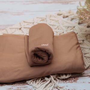 Pu&ograve; includere: Due pezzi di tessuto color cammello, uno arrotolato e l'altro piatto, su una superficie di uncinetto bianca. Il tessuto arrotolato ha la scritta "camel".