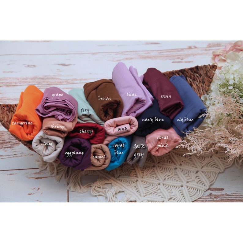 Pu&ograve; includere: Una collezione di 18 campioni di tessuto arrotolati in vari colori, tra cui mandarino, uva, gambero, felce, ciliegia, rosa, nuvola, melanzana, cammello, blu reale, grigio scuro, rosa corallo, blu navy, blu scuro e marrone. I campioni sono disposti in un cesto.