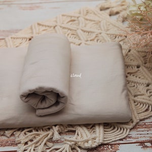 Pu&ograve; includere: Uno sfondo in tessuto beige per la fotografia, arrotolato e posizionato su un tappeto all'uncinetto color crema. Il tessuto &egrave; liscio e ha una lucentezza sottile.