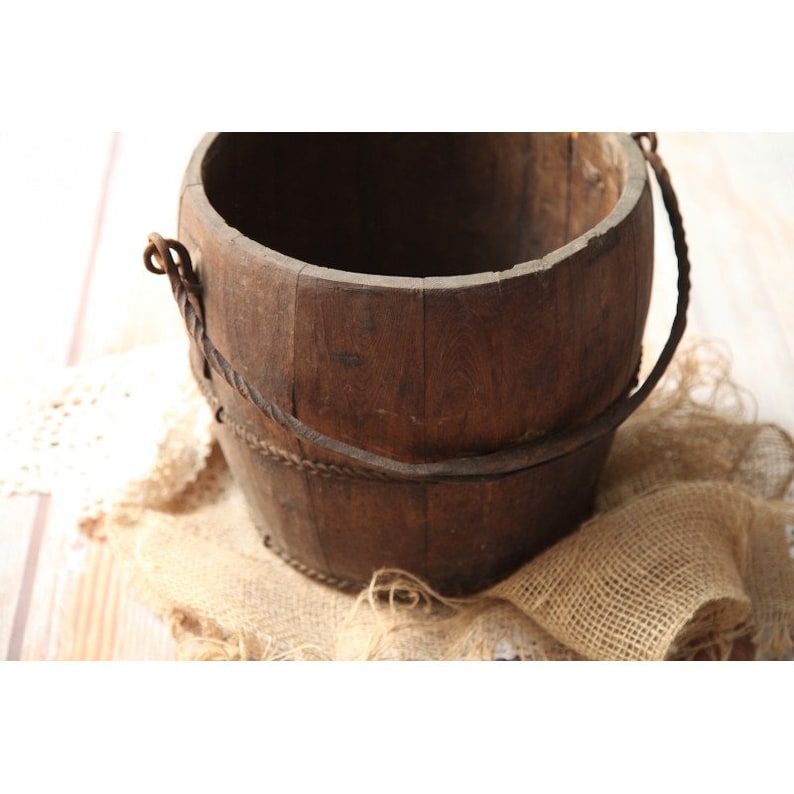 May include: A rustic wooden bucket with a rope handle. The bucket is made of dark brown wood and has a natural, weathered look.