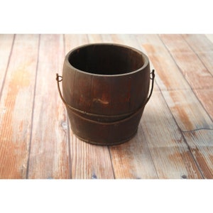 May include: A rustic wooden bucket with a metal handle. The bucket is brown and has a worn, weathered look.