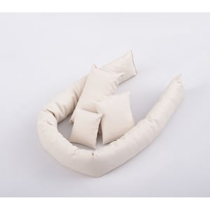 Puede incluir: Un conjunto de cinco almohadas acolchadas de color crema, que incluyen dos almohadas largas y tres almohadas cuadradas más pequeñas. Las almohadas están dispuestas en forma de U.