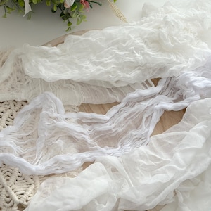 May include: White gauze fabric draped over a wooden tray. The fabric is soft and delicate, with a slightly wrinkled texture.