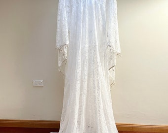 May include: A white lace maxi dress with long sleeves and a V-neckline. The dress has a flowing silhouette and features delicate lace detailing throughout.