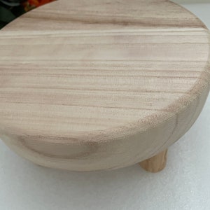 Puede incluir: Un pedestal redondo de madera con un acabado de madera natural y tres patas. El pedestal est&aacute; hecho de madera clara y tiene una superficie lisa.