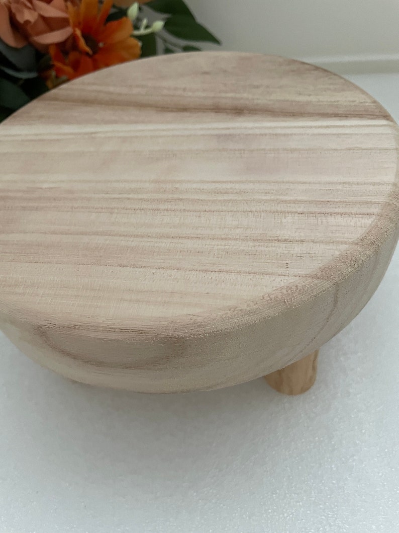 Puede incluir: Un pedestal redondo de madera con un acabado de madera natural y tres patas. El pedestal est&aacute; hecho de madera clara y tiene una superficie lisa.