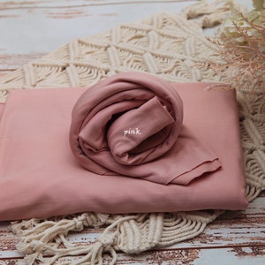 Pu&ograve; includere: Una copertina in tessuto rosa per fasciare i neonati, arrotolata su una superficie di uncinetto bianca. Il tessuto &egrave; morbido e liscio, e la copertina &egrave; perfetta per la fotografia di neonati.
