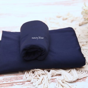 Pu&ograve; includere: Un rotolo di tessuto blu navy con la scritta "navy blue" stampata su di esso. Il tessuto &egrave; piegato a met&agrave; e si trova su una superficie di uncinetto bianca.