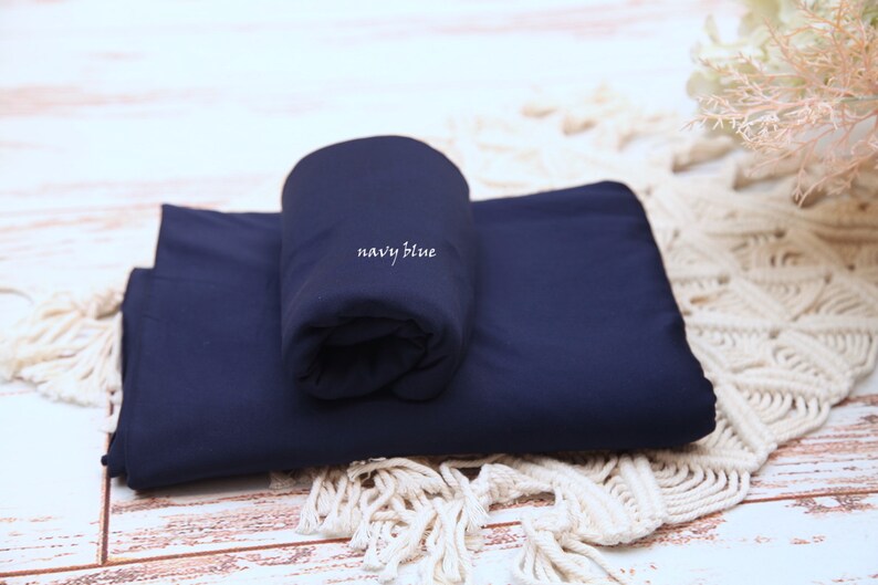 Pu&ograve; includere: Un rotolo di tessuto blu navy con la scritta "navy blue" stampata su di esso. Il tessuto &egrave; piegato a met&agrave; e si trova su una superficie di uncinetto bianca.