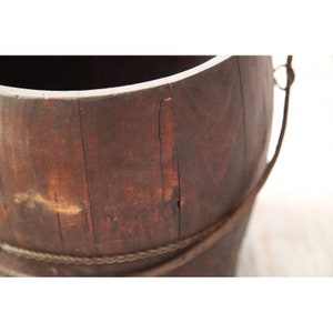 May include: A brown wooden bucket with a rope handle. The bucket is made of wood slats and has a rustic appearance.
