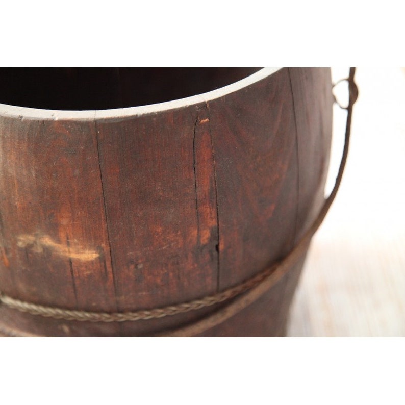 May include: A brown wooden bucket with a rope handle. The bucket is made of wood slats and has a rustic appearance.