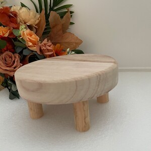 Puede incluir: Un peque&ntilde;o soporte para tartas redondo de madera con tres patas. El soporte est&aacute; hecho de madera natural y tiene un color marr&oacute;n claro.