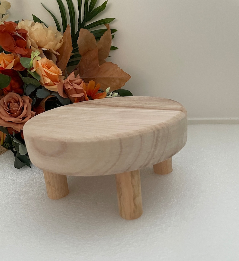 Puede incluir: Un peque&ntilde;o soporte para tartas redondo de madera con tres patas. El soporte est&aacute; hecho de madera natural y tiene un color marr&oacute;n claro.