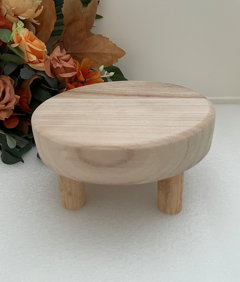 Puede incluir: Un pedestal redondo de madera con tres patas. El pedestal est&aacute; hecho de madera clara y tiene un acabado liso y natural.