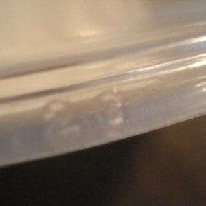 May include: Close-up of the bottom edge of a white ceramic dish. The edge is slightly rounded and has a smooth, glossy finish.
