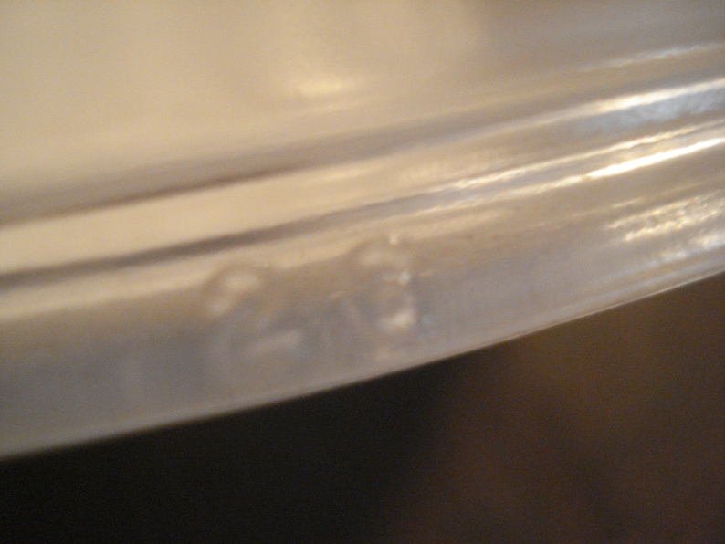 May include: Close-up of the bottom edge of a white ceramic dish. The edge is slightly rounded and has a smooth, glossy finish.