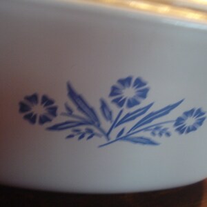 May include: White ceramic baking dish with a blue floral design. The design features three stylized flowers with blue leaves.