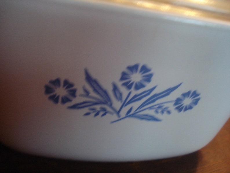 May include: White ceramic baking dish with a blue floral design. The design features three stylized flowers with blue leaves.