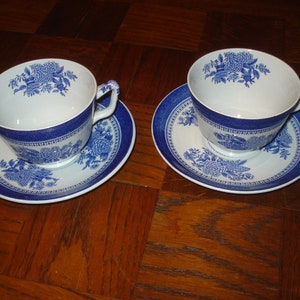May include: Two blue and white teacups and saucers with a floral pattern. The cups and saucers are on a wooden surface.