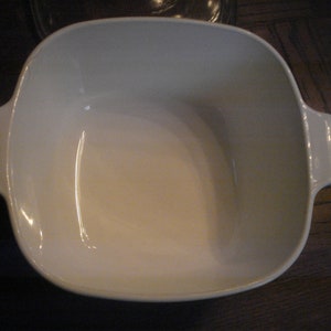 May include: White ceramic baking dish with rounded edges and two handles. The dish is empty.