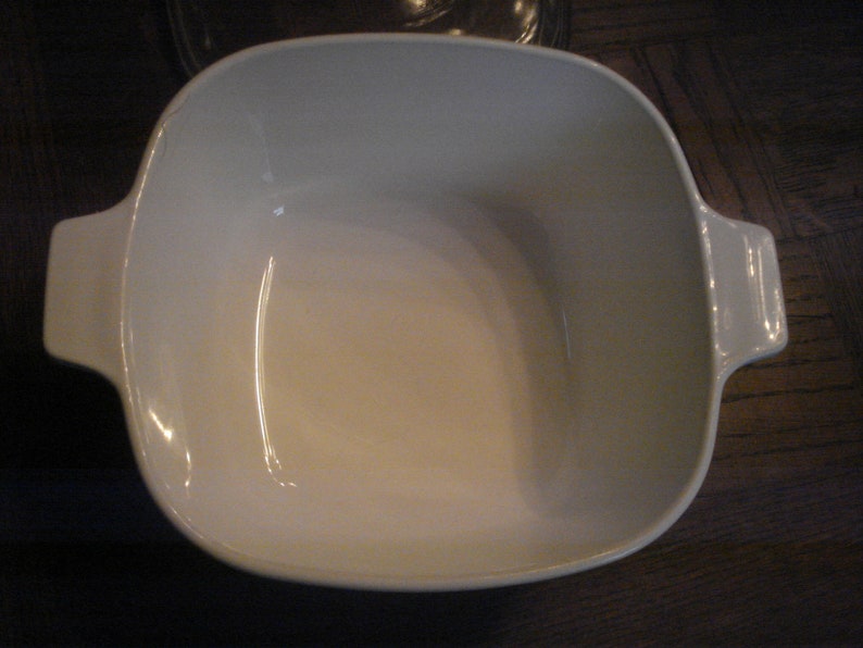 May include: White ceramic baking dish with rounded edges and two handles. The dish is empty.