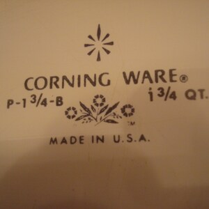 May include: A white Corning Ware baking dish with a black logo and the text "CORNING WARE", "P-1 3/4-B", "1 3/4 QT.", and "MADE IN U.S.A."