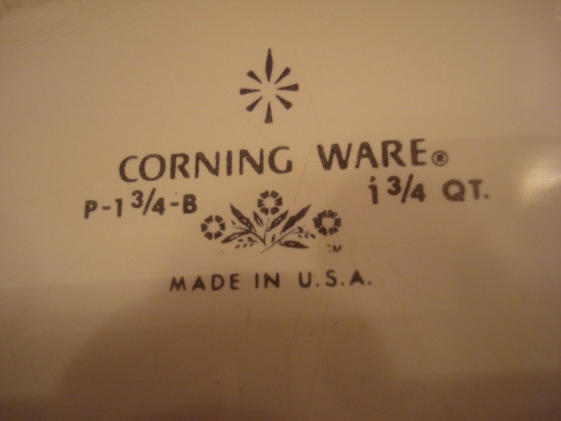 May include: A white Corning Ware baking dish with a black logo and the text "CORNING WARE", "P-1 3/4-B", "1 3/4 QT.", and "MADE IN U.S.A."