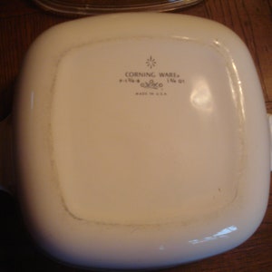 May include: White Corning Ware baking dish with two handles. The dish has a  "Corning Ware" logo with the text "1 1/2 QT" and "Made in U.S.A."