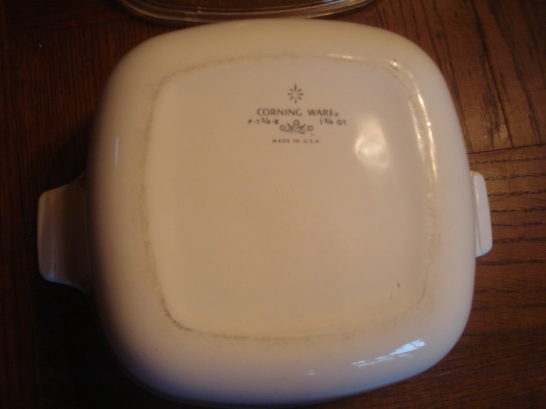 May include: White Corning Ware baking dish with two handles. The dish has a  "Corning Ware" logo with the text "1 1/2 QT" and "Made in U.S.A."