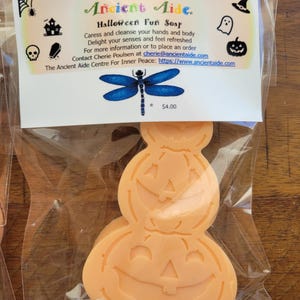 Puede incluir: Jabón divertido de Halloween naranja en una bolsa de plástico transparente. El jabón tiene la forma de una pila de tres calabazas de Halloween. El embalaje incluye el texto "Ancient Aide" y "Halloween Fun Soap".