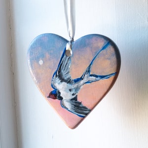 Ceramic heart-shaped decoration. Handpainted swallows. Moonrise, sunset. Pastel colors. Hanging ceramic heart with ribbon. Birds in flight.
