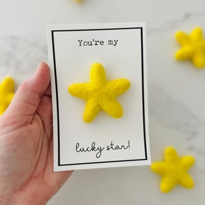 May include: A greeting card with a black border and the text "You're my lucky star!" A yellow felt star is attached to the card. Several yellow felt stars are scattered around the card.