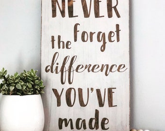 May include: White wooden sign with the text "NEVER forget the difference YOU'VE made" in brown lettering.