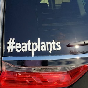 Könnte beinhalten: Ein schwarzes Auto mit einem weißen Aufkleber auf der Heckscheibe, auf dem "#eatplants" steht.