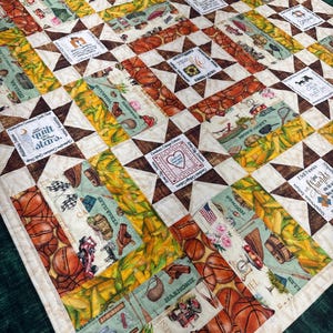 May include: A handmade quilt with a patchwork design. The quilt features star-shaped blocks in brown and cream, interspersed with rectangular panels showcasing basketballs, corn, and various country-themed illustrations. The quilt has a green border.