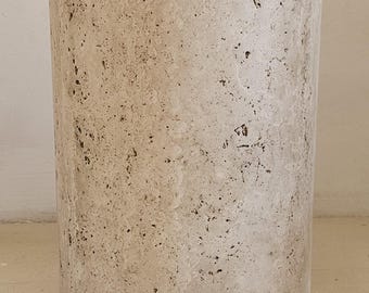 May include: A round, cylindrical, light beige travertine stone side table with a rough, textured surface.