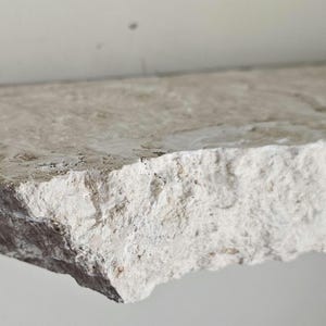 May include: A rough-hewn, light gray stone shelf with a slightly uneven edge. The shelf is made of natural stone and has a rustic, organic look.