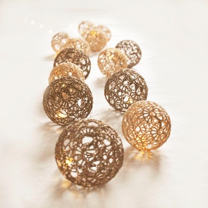 May include: A string of warm white LED lights with a crocheted, beige and brown, ball-shaped cover. The lights are arranged in a curved line on a white surface.