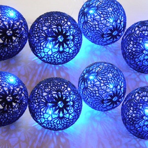 May include: A string of blue crocheted globe lights with a white wire. The globes are illuminated with blue LED lights.
